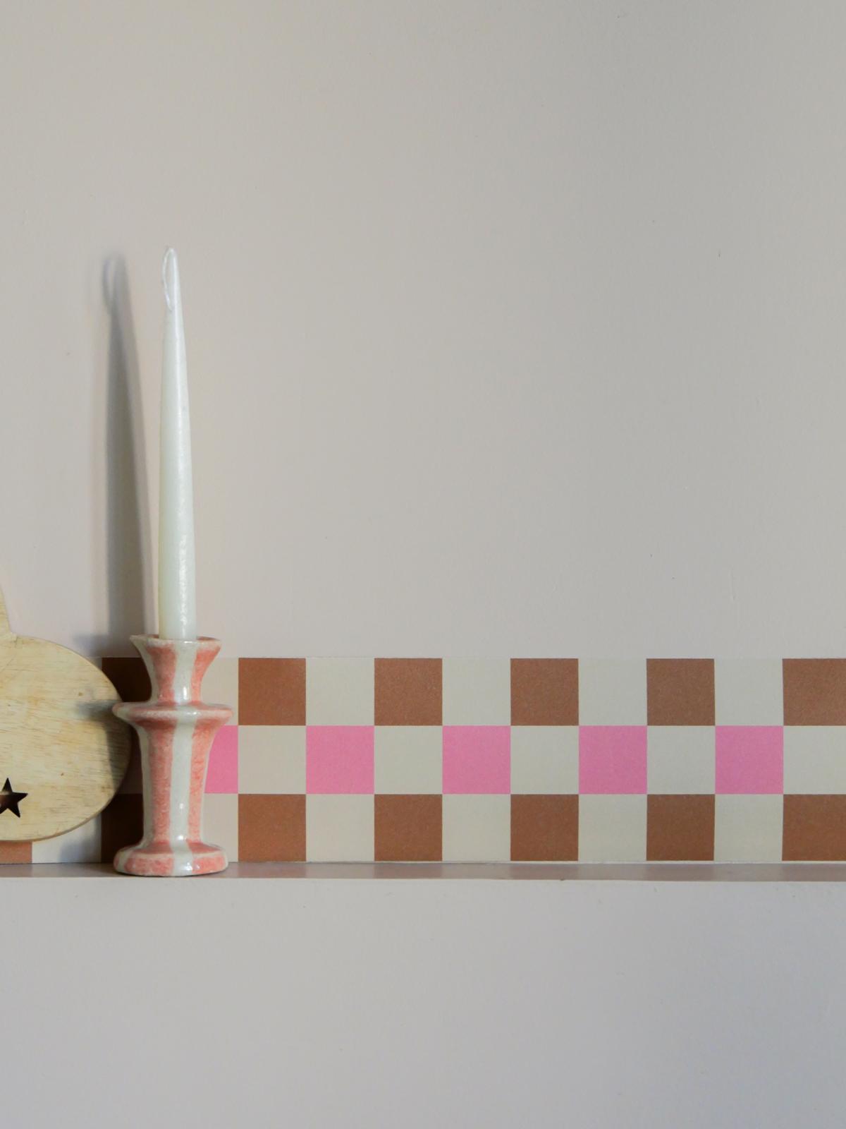 Détail de la frise Cadence Rose près d'un bougeoir en céramique, damier camel et rose poudré sur fond crème — Bilboquet Déco