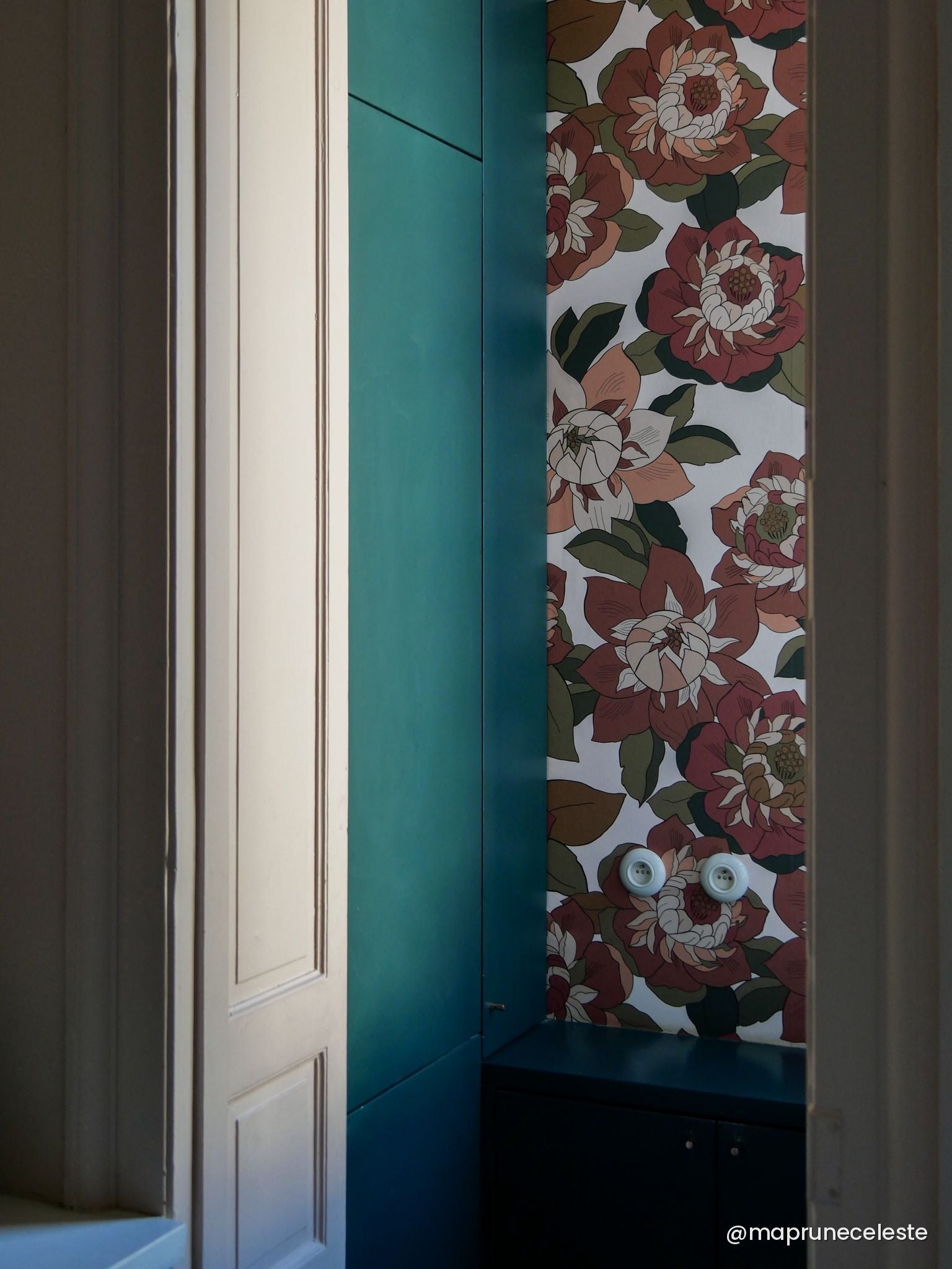 Papier peint Hippie aux grandes fleurs rouge brique et feuillage vert, vu depuis une embrasure aux boiseries crème et bleu canard — Bilboquet Déco

