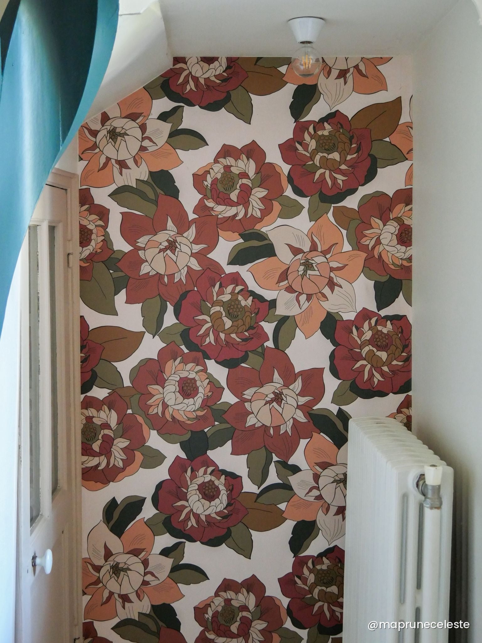 Papier peint Hippie aux grandes fleurs rouge brique et feuillage vert sur un mur sous pente, porte bleu canard — Bilboquet Déco