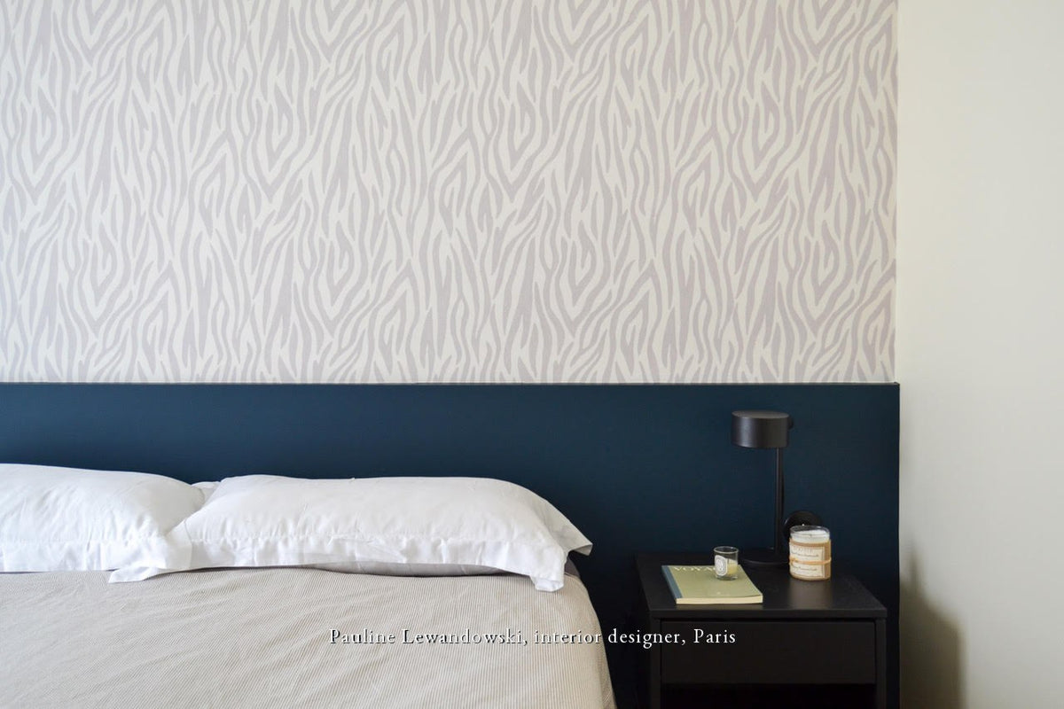 Papier peint Safari gris Bilboquet Déco posé en partie haute au-dessus d'un soubassement bleu profond dans une chambre d'adulte