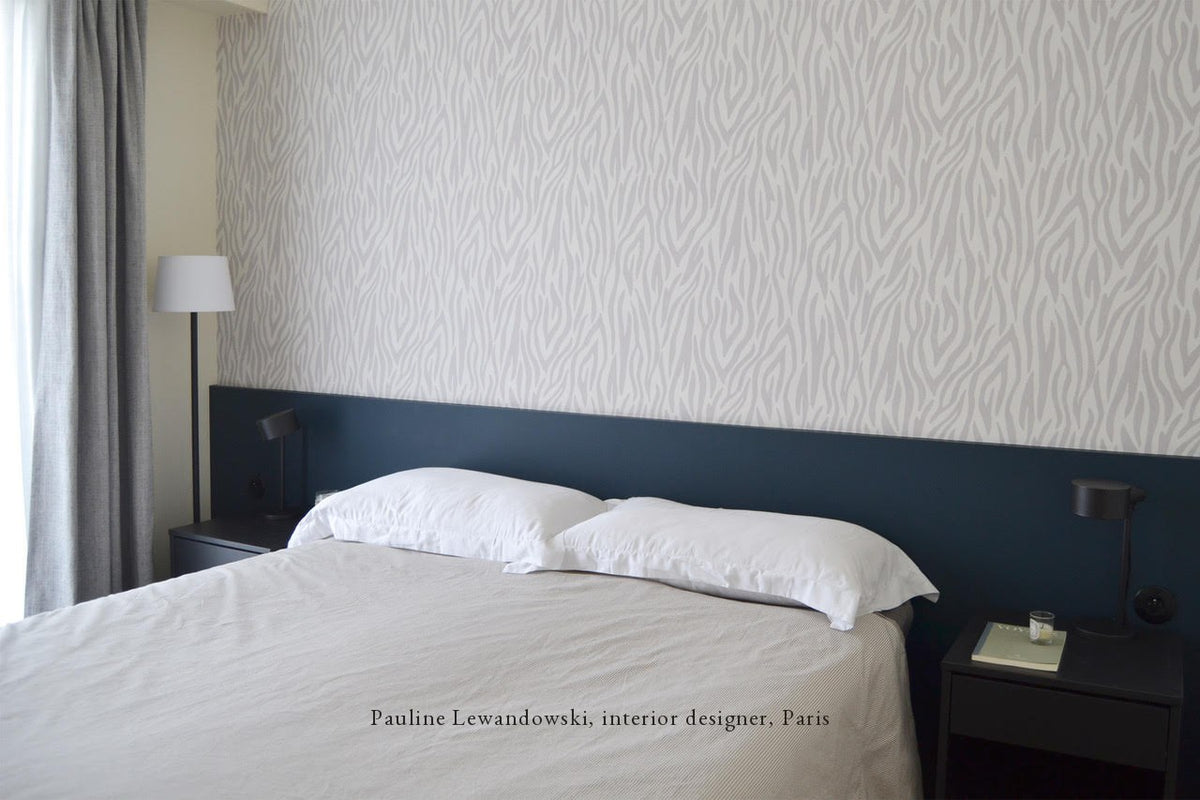 Chambre d'adulte tapissée de papier peint Safari gris Bilboquet Déco, soubassement bleu et linge de lit blanc